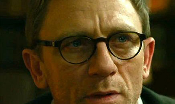 Man in black thick-frame glasses, looking intently ahead.