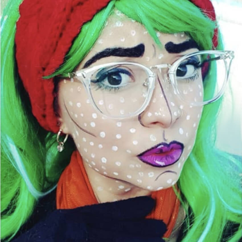 Person with bright green hair, clear glasses, red headband, and comic book style makeup with white dots.
