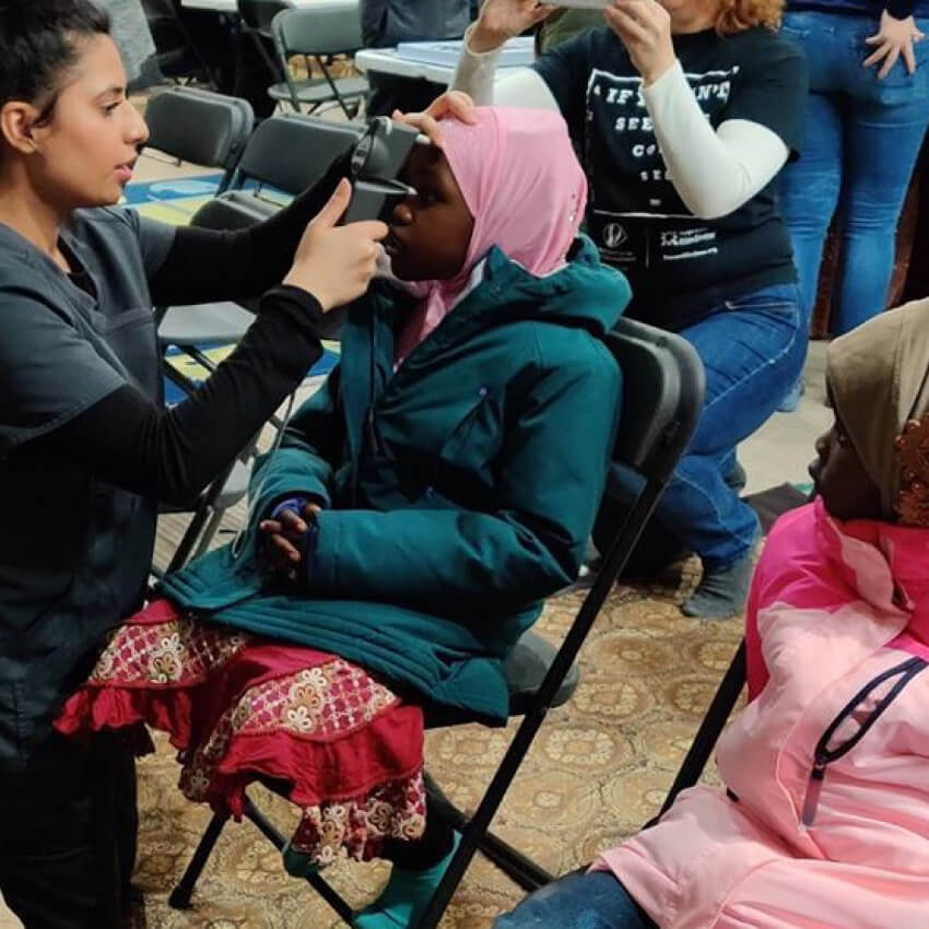 Optometrist examining a girl's eyes with a handheld eye examination device.
