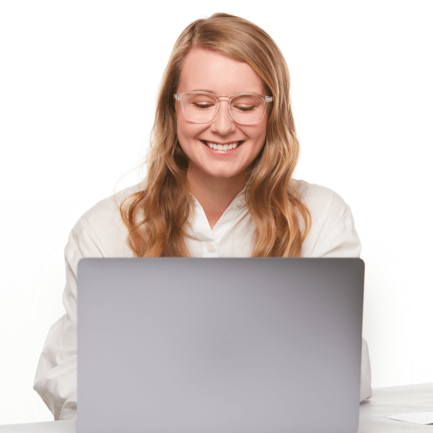 Woman wearing glasses using a laptop, smiling, and wearing a white button-up shirt.