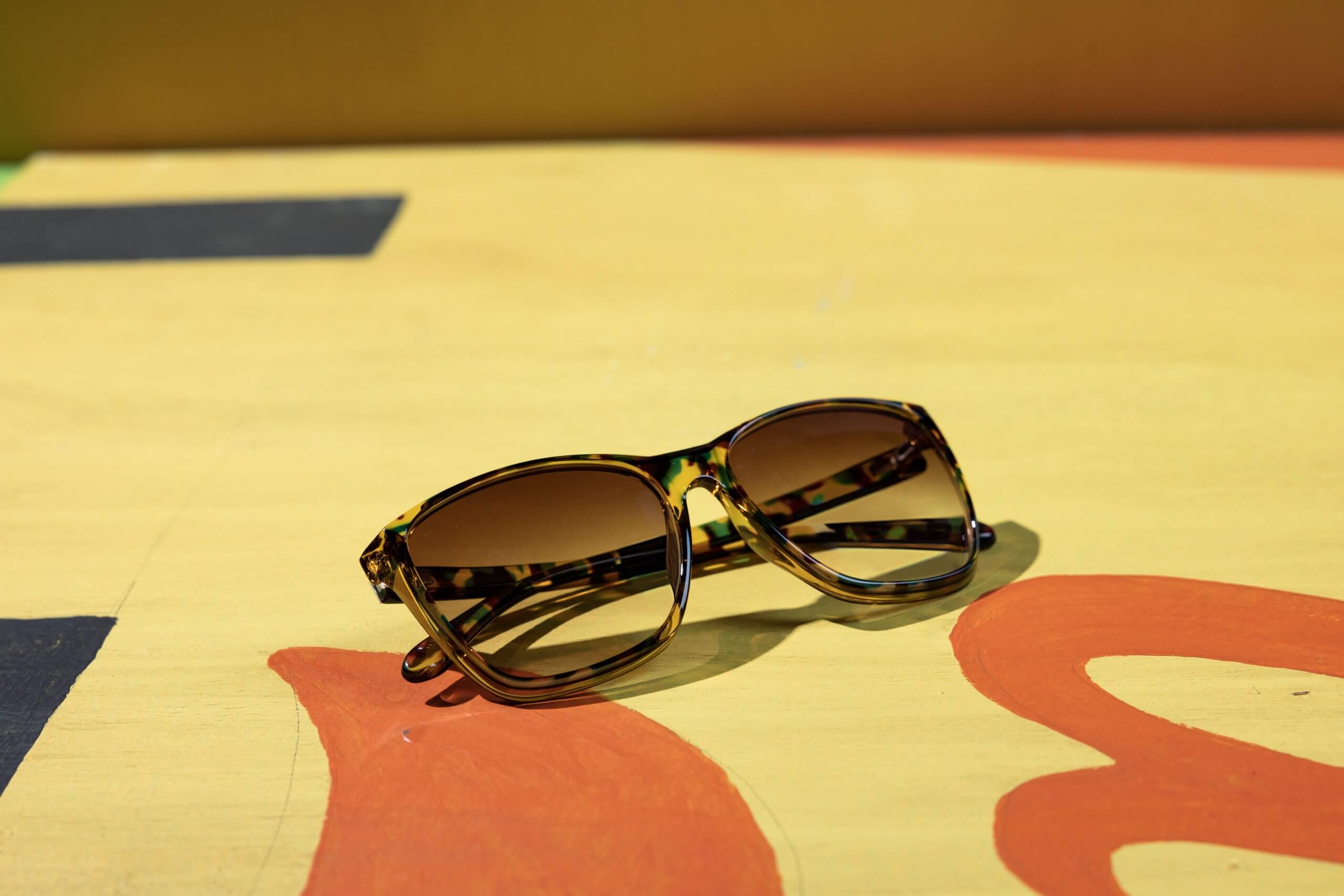 Tortoiseshell frame sunglasses with brown-tinted lenses on a yellow and red surface.