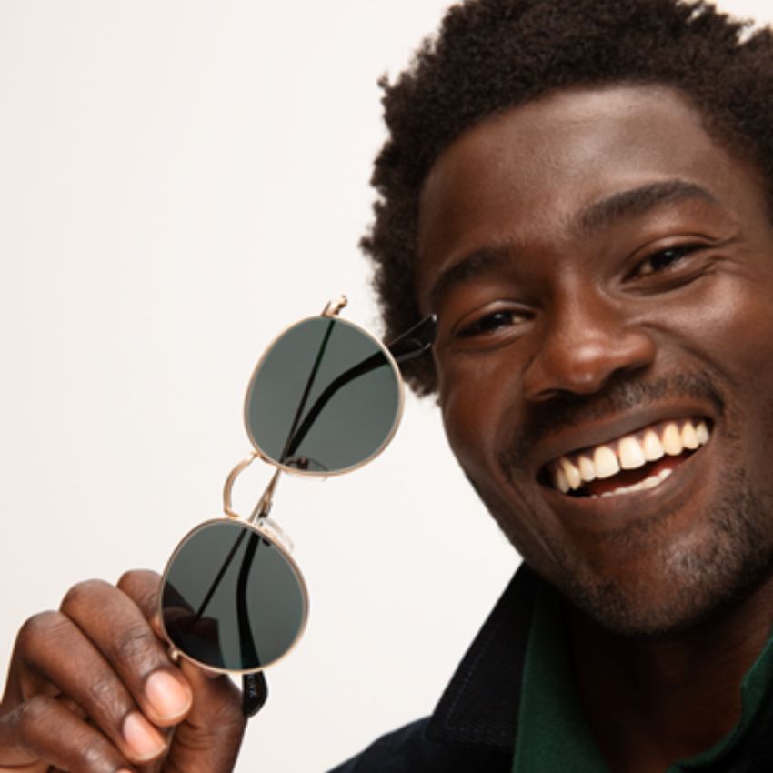 Round sunglasses with dark lenses, held up by a smiling person.