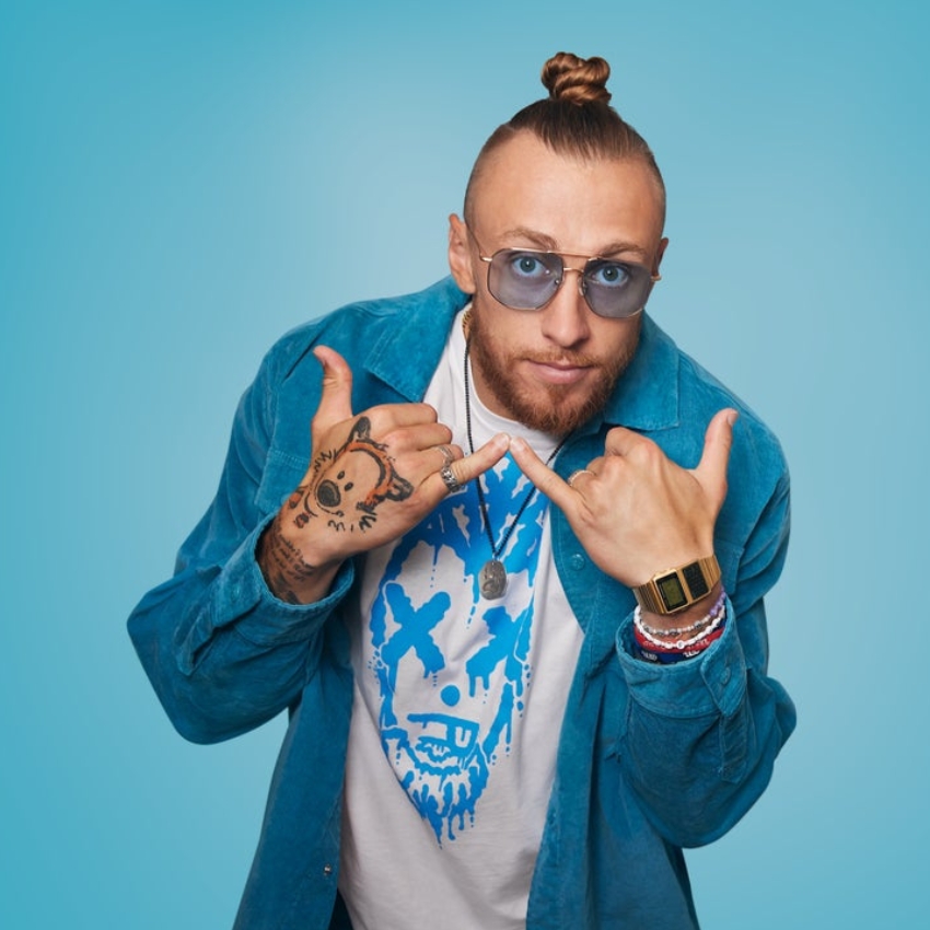 Man wearing sunglasses, blue shirt, graphic T-shirt with blue design, gold watch, and bracelets.
