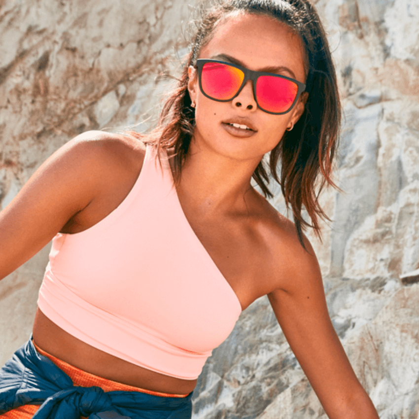Woman wearing a light pink one-shoulder crop top and red mirrored sunglasses.