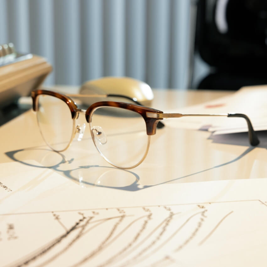 Brown and gold semi-rimless eyeglasses with clear lenses placed on a desk with documents underneath.