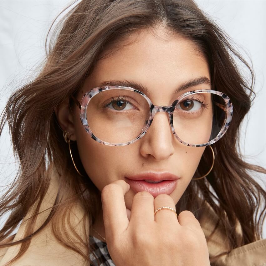 Woman wearing round, tortoiseshell glasses with light pink, black, and white hues.