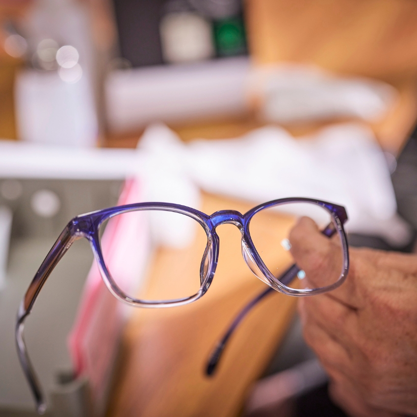 Hand holding blue and clear eyeglasses by the temple in focus.