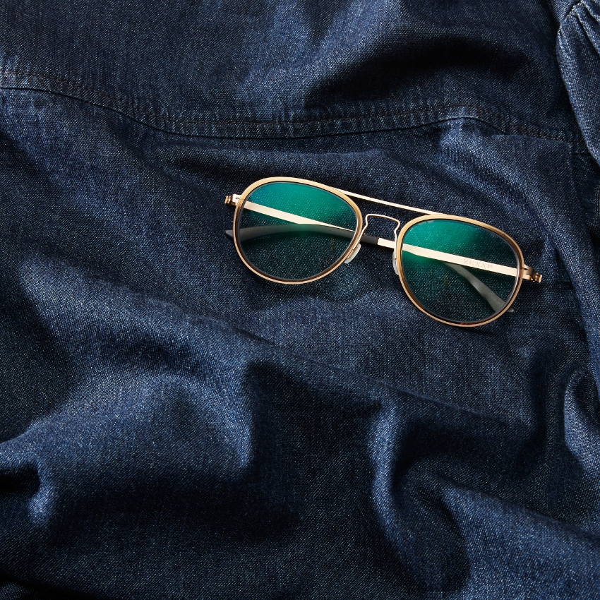 Gold-framed aviator sunglasses with green-tinted lenses on dark blue denim fabric.