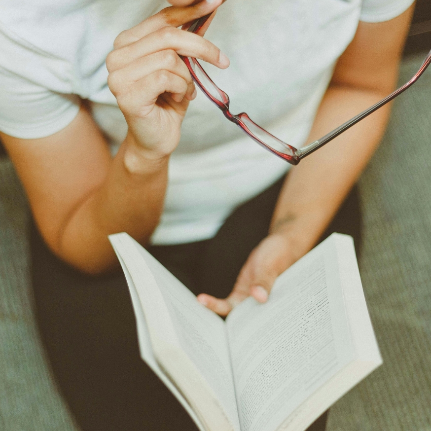 Person holding eyeglasses while reading a book.