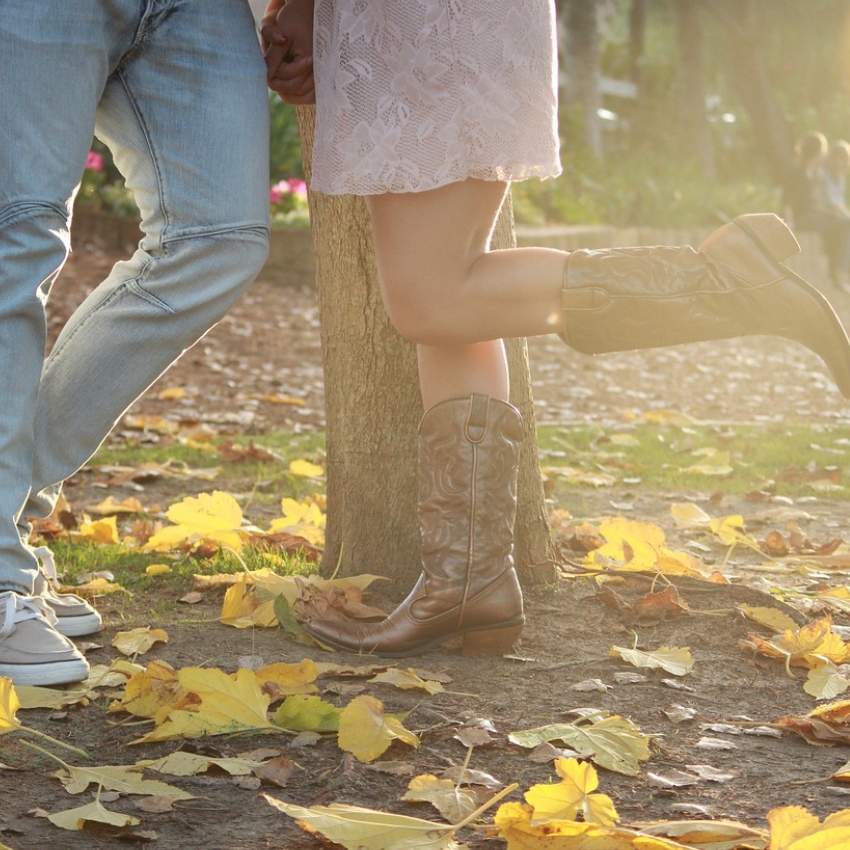 Brown leather cowboy boots worn by a woman in a pink lace dress, standing beside a person in jeans.