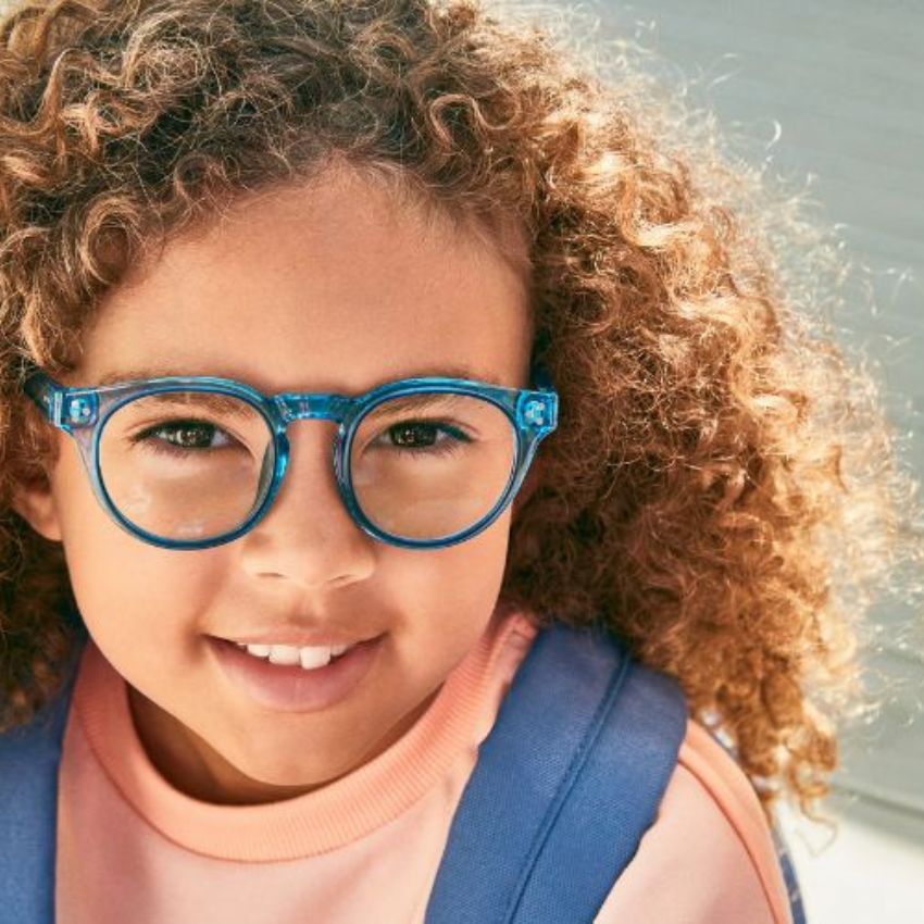 Child wearing round blue glasses and a light pink shirt with a blue overall.